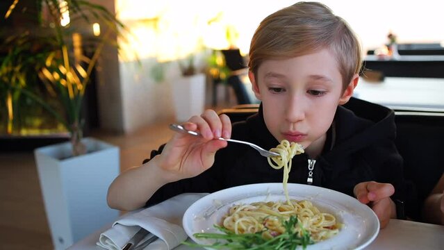 a child in a restaurant on a fork with carbonara pasta and eats it
