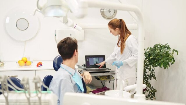 Young female dentist pointing at x-ray and recommending dental treatments to male patient