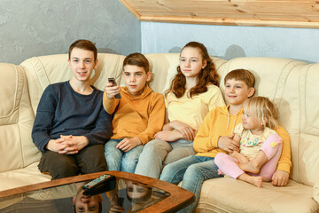 Five children watch TV and switch channels with a remote control