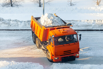 A big orange truck takes snow off the road. Cleaning and cleaning of roads in the city from snow in...