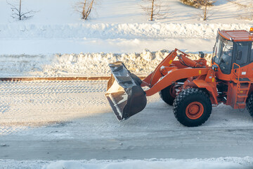 Big orange tractor cleans up snow from the road and loads it into the truck. Cleaning and cleaning...
