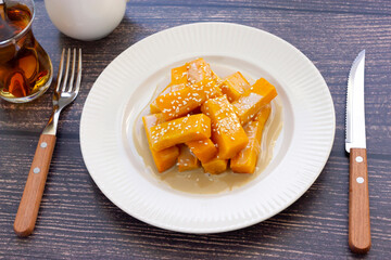 Kabak tatlisi is a traditional Turkish dessert made of pumpkin, sugar, covered tahini sauce, served on white plate, top view with fork, glass of black tea, knife and white gravy boat. Easy to cook. 