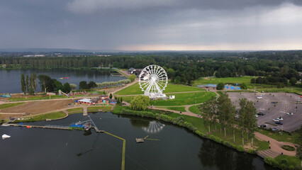 A big Ferris wheel in the small amusement park on the coast of the lake on a gloomy day - Powered by Adobe
