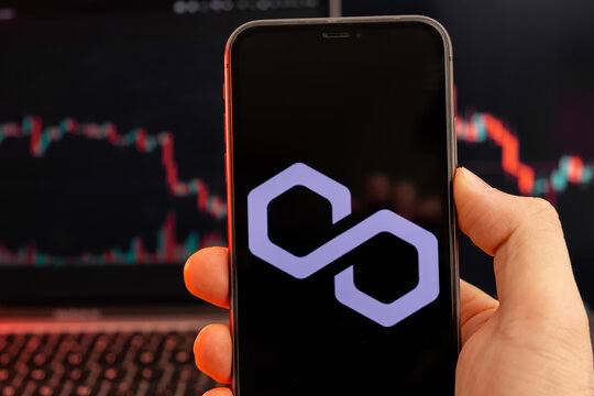 Polygon MATIC cryptocurrency logo on the screen of smartphone in mans hand with downtrend on the chart on a red light background, February 2022, San Francisco, USA.