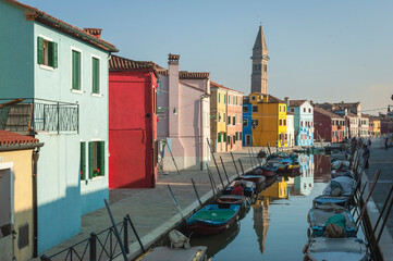 Fototapeta na wymiar Burano, Venezia. Canale con barche da pesca, fondamenta e case colorate riflesse, al tramonto