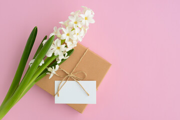 White spring flower and gift box with blank card on pink background, copy space. Woman's day composition, Mother's day card