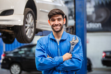 Portrait of smiling male mechanic technician holding wrench in arms crossed at auto garage. repair...