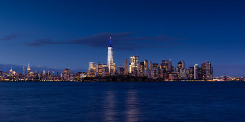New York City Lower Manhattan cityscape in evening. View of  Financial District skyscrapers with World Trade Center, Midtown West and Ellis Island - obrazy, fototapety, plakaty