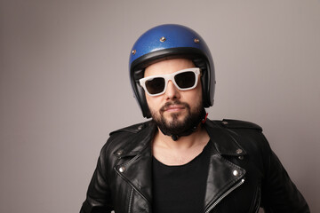 Bearded biker man posing in leather jacket and blue motorcycle helmet.