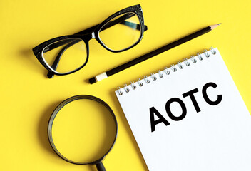 acronym AOTC American Opportunity Tax Credit in notebook with pencil, magnifier, and glasses on a yellow background