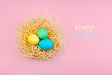 Fototapeta na wymiar Easter eggs painted in pastel colors in hay nest against a pink background.