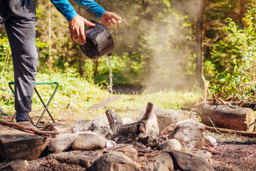 Man extinguishing campfire with water from cauldron in summer forest. Put out campfire. Traveling fire safety rules - obrazy, fototapety, plakaty