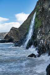 Tresaith Waterfall, dropping off high cliffs into turbulent sea, Tresaith beach in Ceredigion, Wales