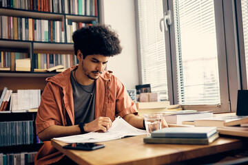 Young Muslim man studies while preparing for upcoming exams in library at the university.