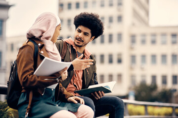 Young Muslim student and his female friend talk while studying together outdoors.