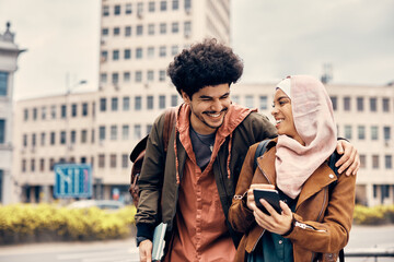 Cheerful Muslim university friends laugh and have fun while using smart phone in the city.