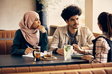 Young Muslim college student and his female friends talk while learning together in cafe.