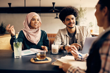 Group of happy Muslim college friends talk while learning together in cafeteria.