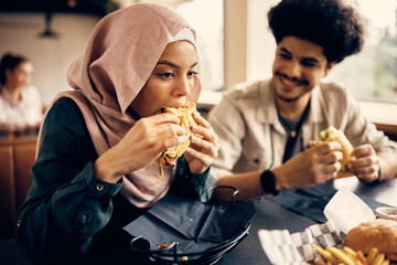 Young Muslim woman eats with friends on lunch break in cafeteria.