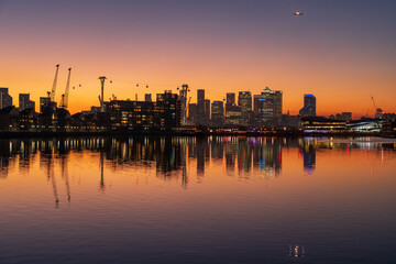 Sunset over the London skyline with orange sky reflecting in the water.