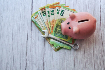 Ein Stapel Geldscheine mit Schraubenschlüssel und Sparschwein auf Holzuntergrund, horizontal   
