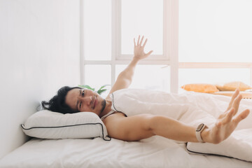 Obraz na płótnie Canvas Asian man just wake up in a happy morning in bright white bedroom.
