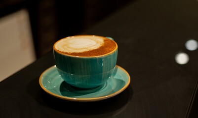 Selective focus. A cup of cappuccino ceramic turquoise stands on the table. Dark photo