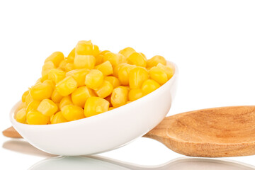 Bright yellow canned corn kernels in white ceramic saucer with wooden spoon, macro, isolated on white background.