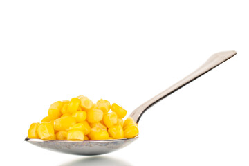 Bright yellow canned corn kernels with metal spoon, macro, isolated on white background.