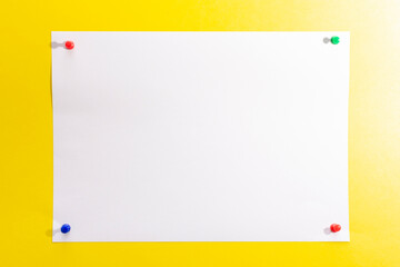 empty white sheet of paper pinned with push pins on a yellow background