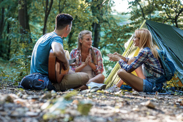 Group of friends sitting and relaxing in front of the camping tent.	
