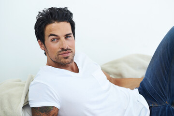 Hes go that casual charm. Shot of ruggedly handsome man wearing a white t-shirt and lying on a bed. - Powered by Adobe