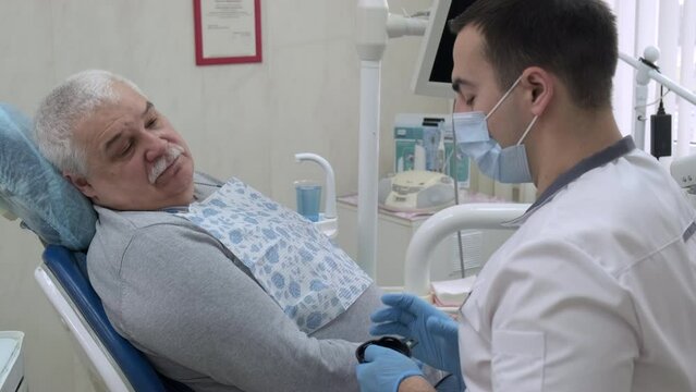 Male dentist consulting elderly patient before treatment in dental clinic. Doctor communicates with patient. Dentist explaining removable dentures to senior man. Healthcare and dentistry business