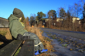 Boy with green hat sitting down. Nice weather a winter day. Close up and isolated. Slight blurred background. Outdoor photo. Stockholm, Sweden.