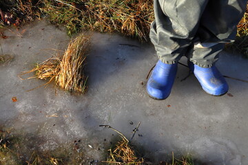 Blue rubber boots on ice. Child walking or standing. Faceless photo. Winter day. Stockholm, Sweden.