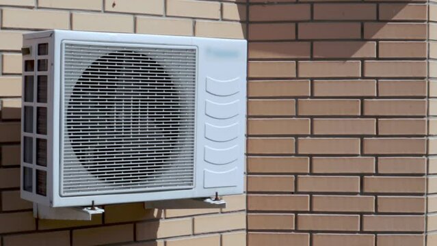 Close-up of a modern climate control unit against the background of a brick wall of the facade of the house from the outside. Wall air conditioner. Air compressor.