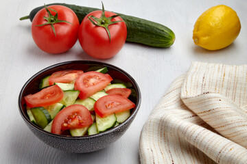 Fresh tomato and cucumber salad in dark bowl and kitchen napkin