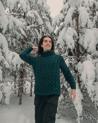 A young guy in a green sweater plays snowballs in a snowy forest