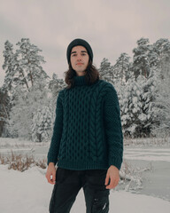 A young guy in a green sweater walks through a snowy forest