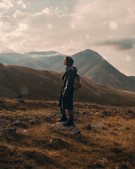 A young guy in a green raincoat walks among the mountains