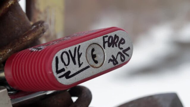 The inscription in English love forever on a red padlock. The locked love padlocks attached to the bridge symbolize unbreakable love. Hand shot.
