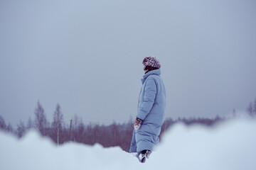 Fototapeta na wymiar A young attractive lady is standing on a snowy field near the forest.