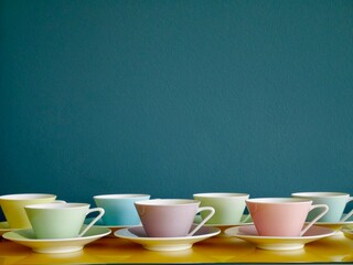 Row of vintage pastel coffee cups on yellow table against petrol background. Afternoon tea party.
