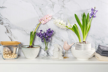 White hyacinth in a large porcelain bowl, figurines of hares and a bird, are on the fireplace against the white marble wall. Layout. Spring concept
