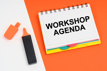 On a white-orange surface lies a marker and a notepad with the inscription - WORKSHOP AGENDA