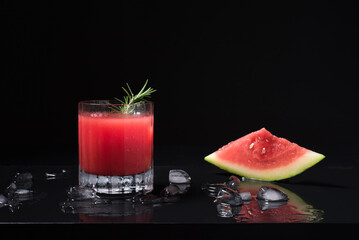 Un vaso de refrescante jugo de sandía triturado adornado con trozos de sandía sobre hielo picado. Cóctel de frutas en fondo negro	