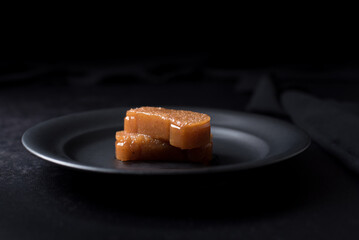 Dulce pasta de gelatina de membrillo dorado sobre una placa de madera negra	