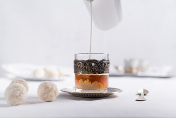 Verter leche en un vaso de té clásico con dulces chocolates blancos cubiertos de coco en el cuadro blanco	