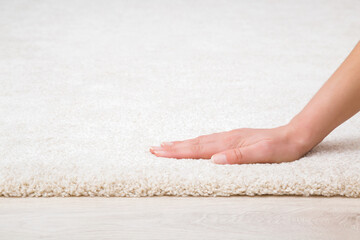 Young adult woman hand touching new white fluffy carpet surface on laminate floor. Closeup....