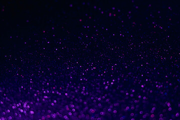 Glitter background. Bokeh light. Defocused round sparks. Blur neon fluorescent blue purple pink color grain texture glow on dark black shimmering abstract overlay.
